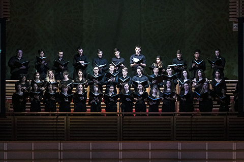 A chorus all dressed in black are holding up books while they are singing